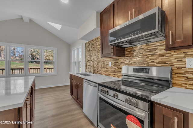 kitchen featuring sink, light stone counters, stainless steel appliances, vaulted ceiling with skylight, and backsplash