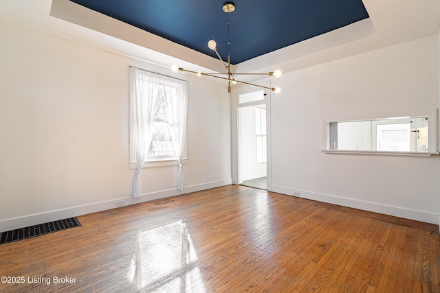 spare room with a raised ceiling, hardwood / wood-style floors, and a notable chandelier