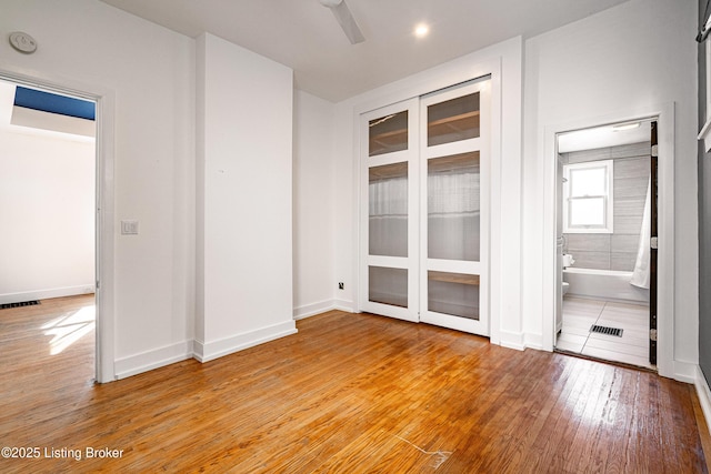 unfurnished bedroom with ensuite bath and wood-type flooring