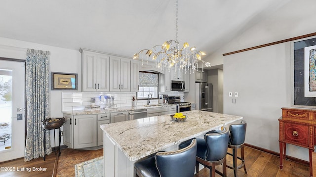 kitchen featuring a center island, lofted ceiling, hanging light fixtures, appliances with stainless steel finishes, and a sink