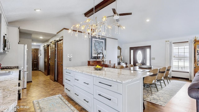 kitchen featuring lofted ceiling with beams, light stone counters, white cabinets, stainless steel microwave, and pendant lighting