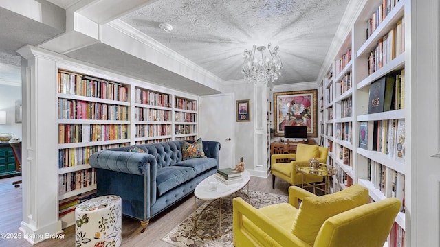 living area with ornamental molding, wood finished floors, wall of books, a textured ceiling, and a chandelier