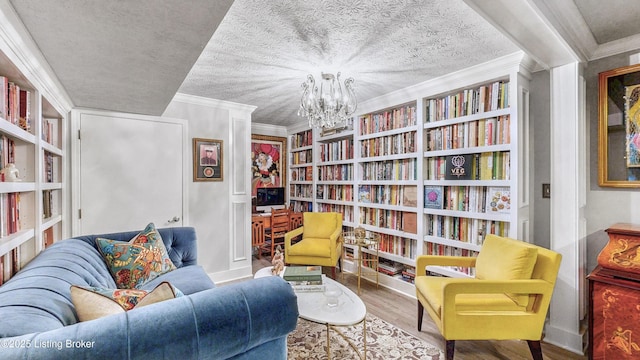 living area with bookshelves, ornamental molding, a textured ceiling, wood finished floors, and a chandelier