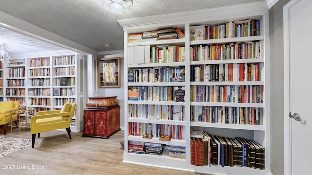 sitting room with a textured ceiling, bookshelves, and wood finished floors