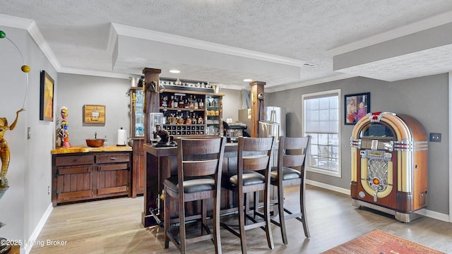 bar with a textured ceiling, indoor bar, baseboards, light wood-style floors, and crown molding