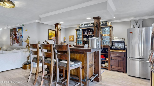 kitchen with light wood-style flooring, a kitchen breakfast bar, freestanding refrigerator, crown molding, and ornate columns