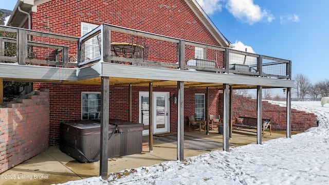 snow covered house with brick siding, a patio area, a balcony, and a hot tub