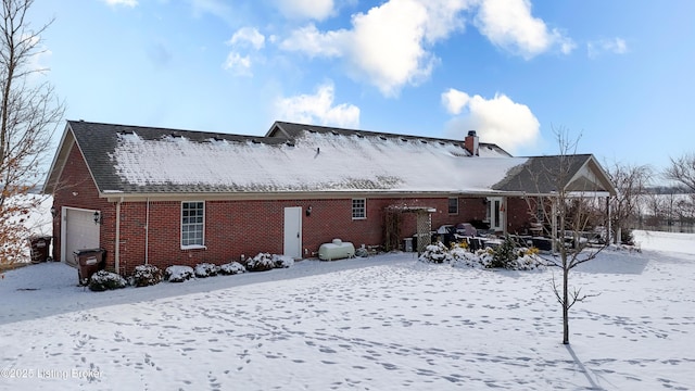 snow covered property with brick siding and a chimney