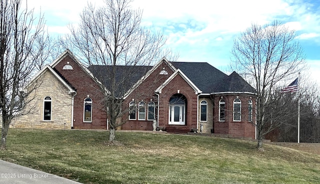 view of front of house featuring stone siding, roof with shingles, a front lawn, and brick siding