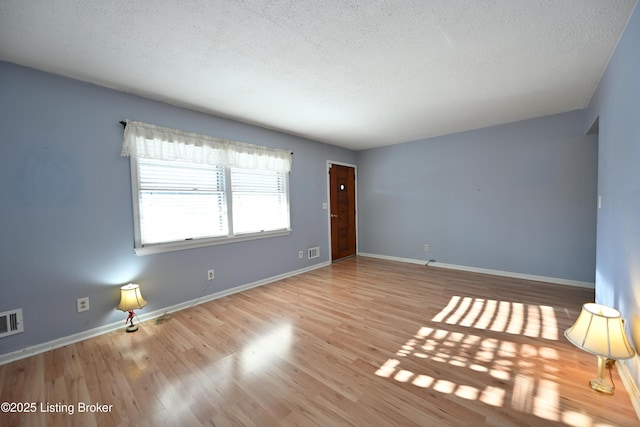 empty room with a textured ceiling, light wood-type flooring, visible vents, and baseboards