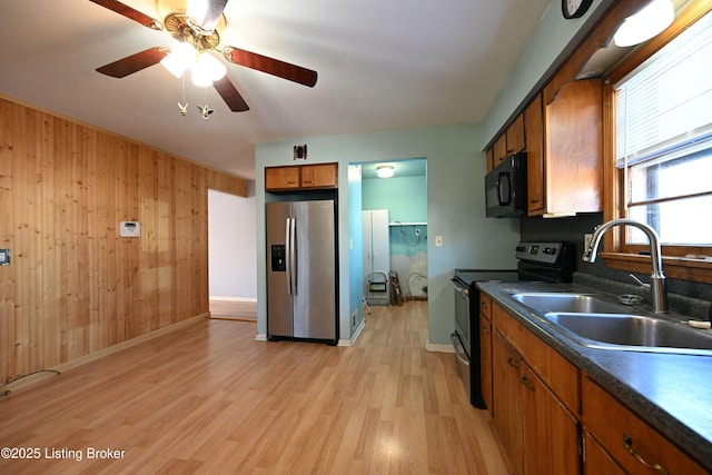 kitchen featuring wooden walls, a sink, appliances with stainless steel finishes, brown cabinetry, and dark countertops