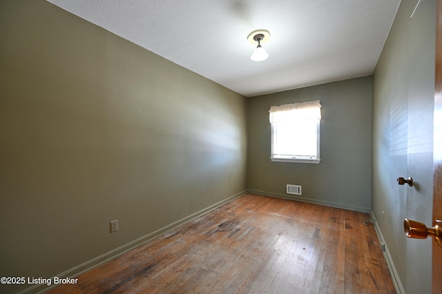 spare room featuring visible vents, baseboards, and wood finished floors