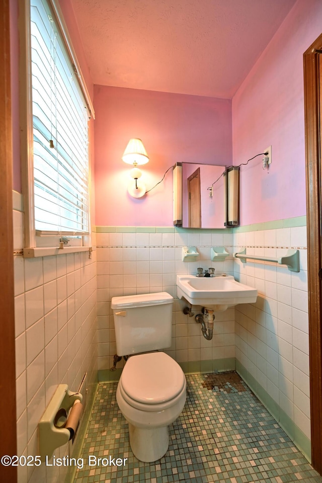 bathroom featuring toilet, a wainscoted wall, a sink, tile walls, and tile patterned floors