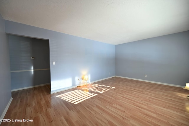 empty room featuring light wood-style floors, baseboards, and a textured ceiling