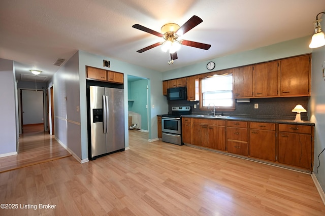 kitchen with light wood finished floors, dark countertops, appliances with stainless steel finishes, brown cabinetry, and a sink