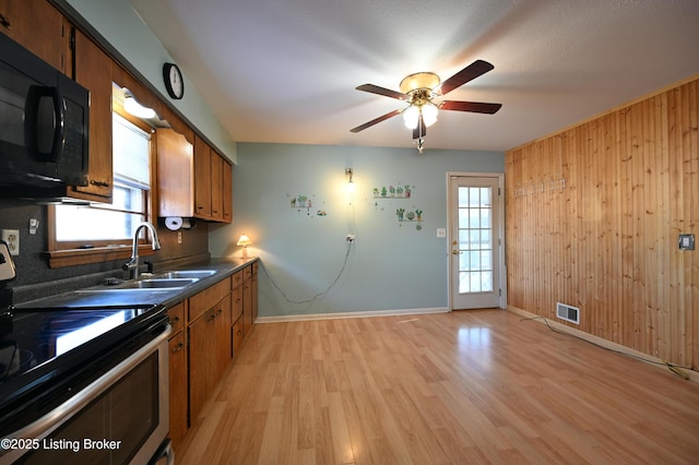 kitchen featuring black microwave, a sink, stainless steel range with electric cooktop, brown cabinetry, and dark countertops