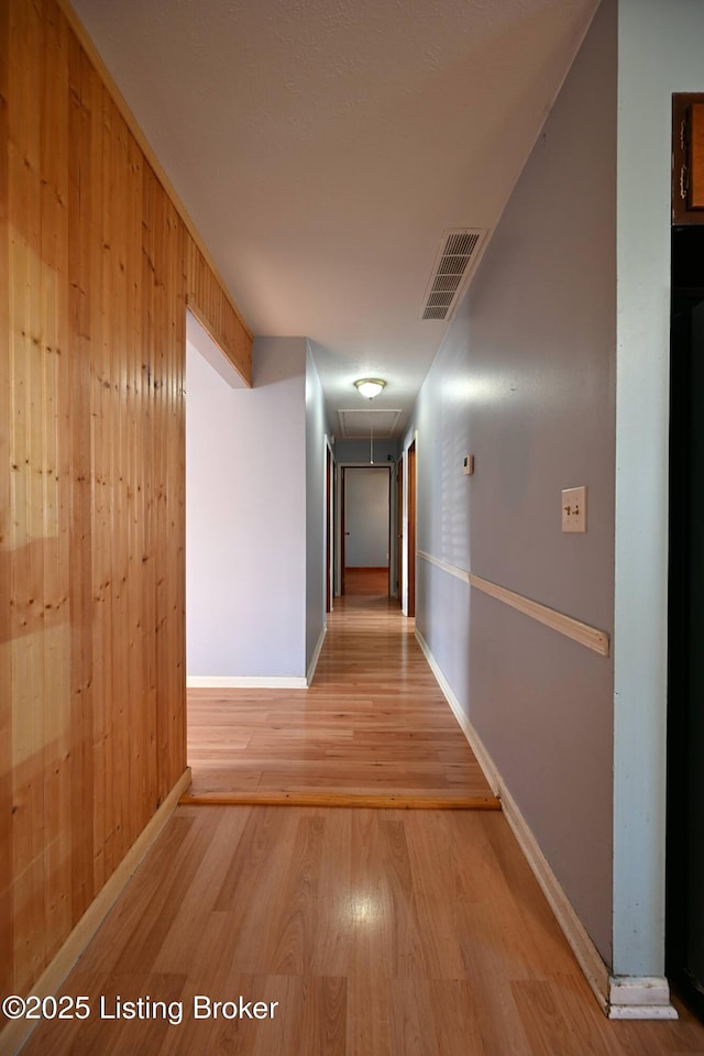 hallway featuring visible vents, light wood-style flooring, attic access, wooden walls, and baseboards