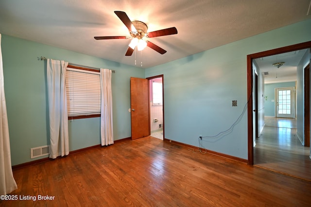 unfurnished bedroom featuring multiple windows, wood finished floors, visible vents, and attic access