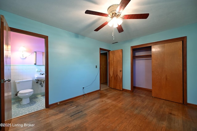 unfurnished bedroom with connected bathroom, wood finished floors, visible vents, tile walls, and a closet