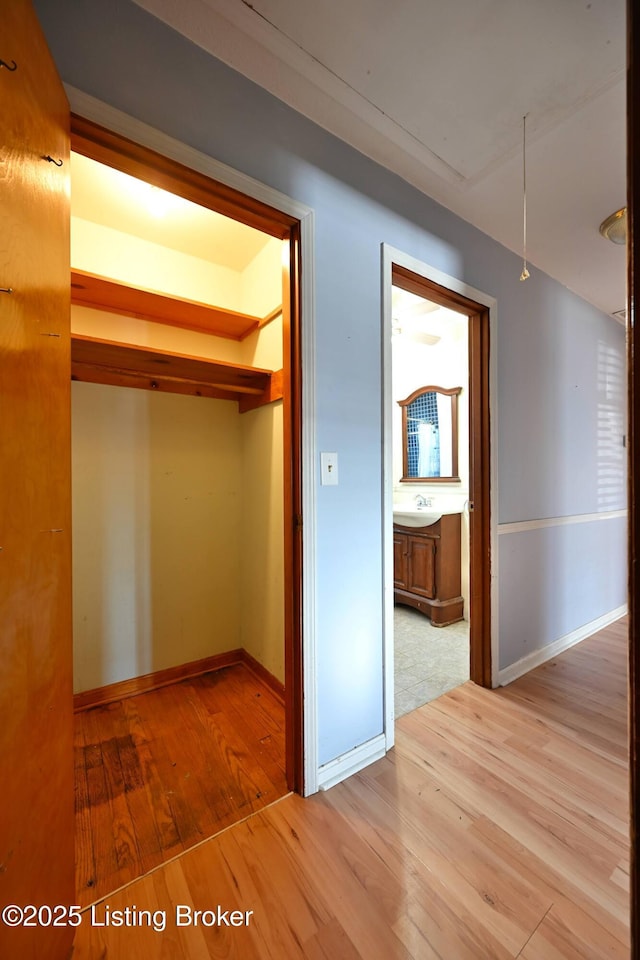 hallway featuring attic access, light wood-style flooring, and baseboards