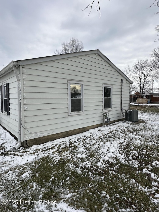 snow covered rear of property featuring central AC