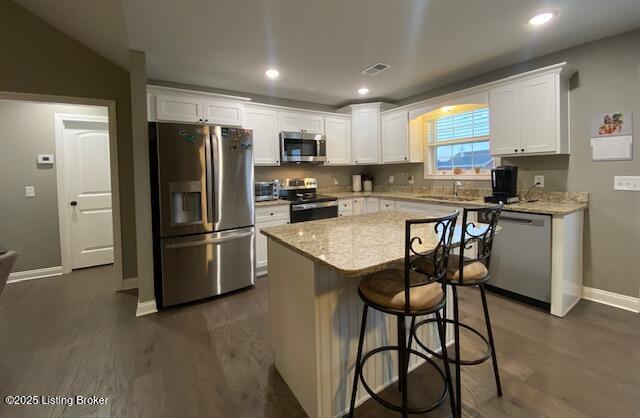 kitchen featuring white cabinetry, appliances with stainless steel finishes, a center island, and light stone countertops