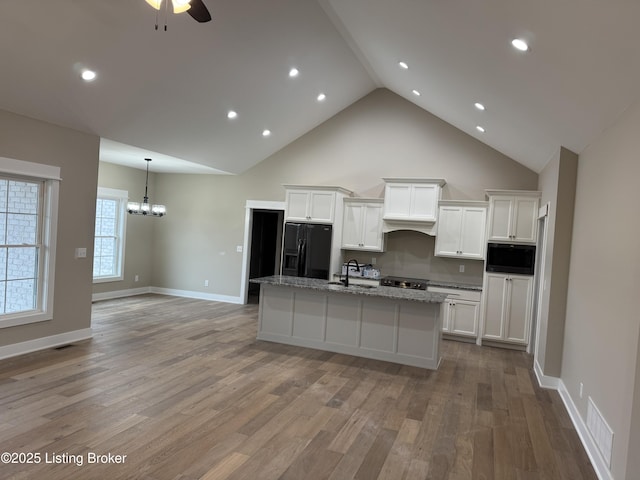 kitchen featuring sink, black appliances, white cabinets, a center island with sink, and light wood-type flooring