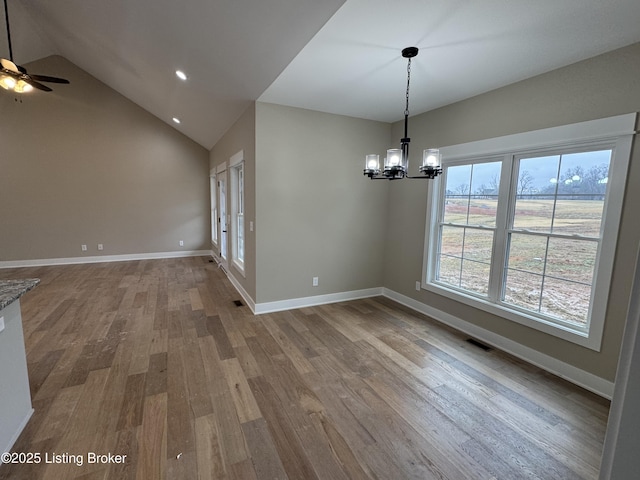 unfurnished dining area featuring ceiling fan with notable chandelier, wood-type flooring, and vaulted ceiling