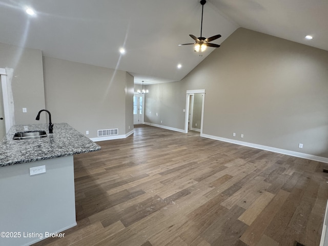 unfurnished living room featuring hardwood / wood-style flooring, sink, ceiling fan with notable chandelier, and high vaulted ceiling