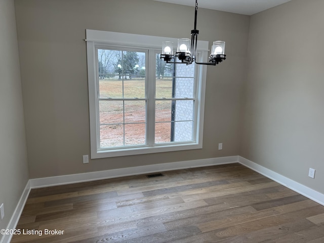 unfurnished dining area with a wealth of natural light, hardwood / wood-style floors, and an inviting chandelier