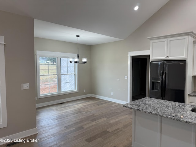 kitchen with black fridge with ice dispenser, light stone counters, decorative light fixtures, vaulted ceiling, and white cabinets