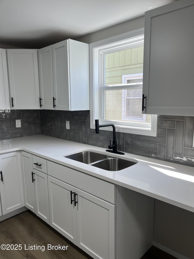 kitchen with light countertops, a sink, white cabinets, and decorative backsplash