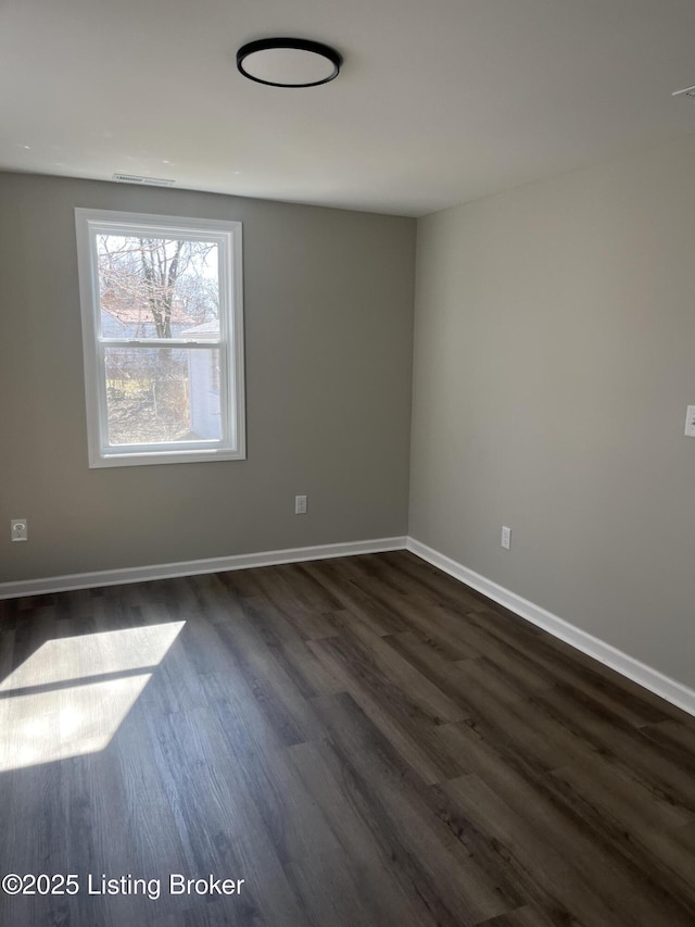 spare room with dark wood-type flooring, visible vents, and baseboards