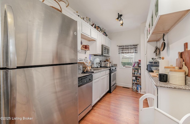 kitchen with stainless steel appliances, light wood-style floors, glass insert cabinets, white cabinetry, and light stone countertops