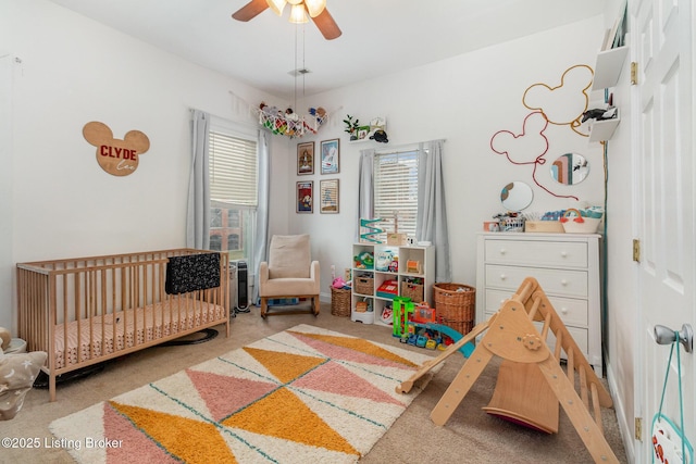 bedroom featuring a nursery area, carpet flooring, and a ceiling fan