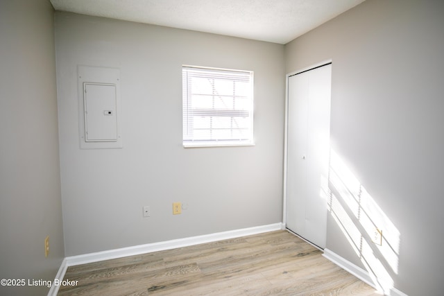 unfurnished room with a textured ceiling, light wood-type flooring, electric panel, and baseboards