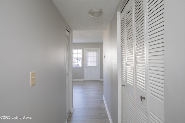 corridor featuring a textured ceiling, wood finished floors, and baseboards