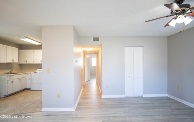 kitchen with a sink, visible vents, white cabinetry, light countertops, and washer / dryer