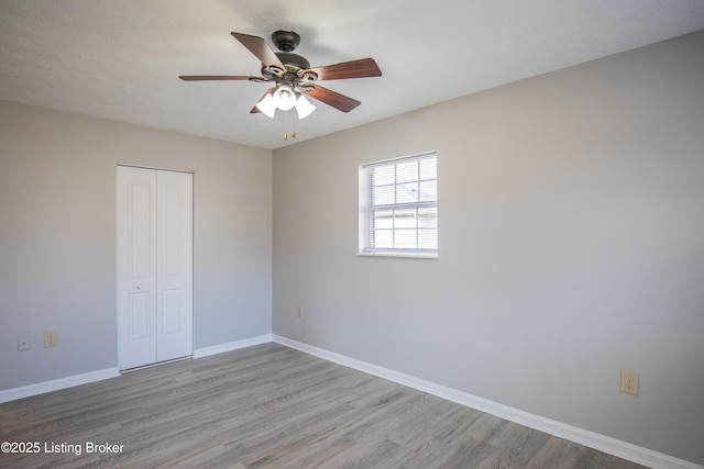 unfurnished bedroom with a ceiling fan, baseboards, a closet, and wood finished floors