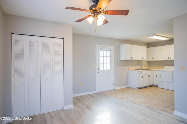 kitchen with a sink, white cabinetry, baseboards, light countertops, and light wood-type flooring