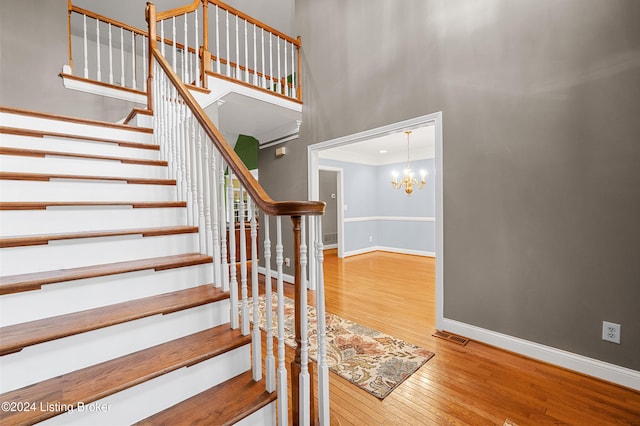 stairway with a chandelier, wood finished floors, a towering ceiling, and baseboards