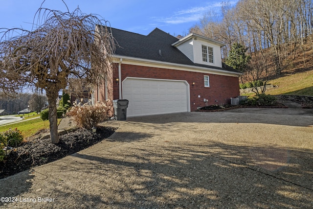 view of side of property with driveway, a shingled roof, an attached garage, central air condition unit, and brick siding