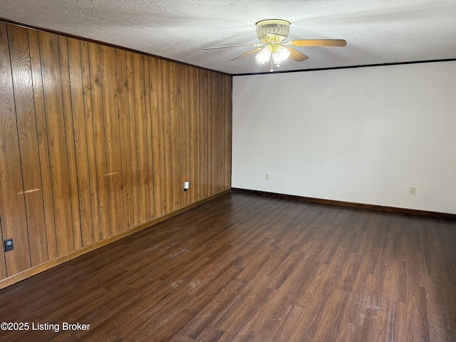 spare room featuring crown molding, dark wood-type flooring, ceiling fan, wooden walls, and a textured ceiling