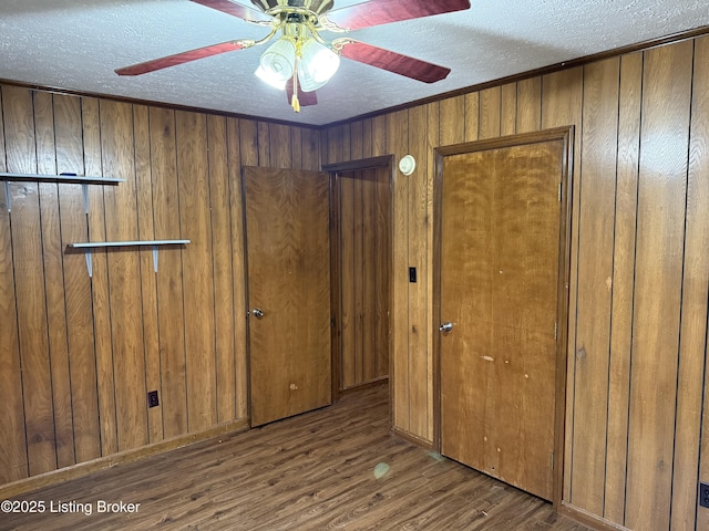 empty room featuring crown molding, a textured ceiling, wooden walls, dark hardwood / wood-style floors, and ceiling fan