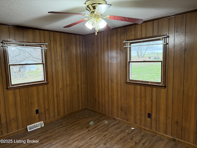 unfurnished room featuring ceiling fan, dark hardwood / wood-style floors, wooden walls, and a textured ceiling