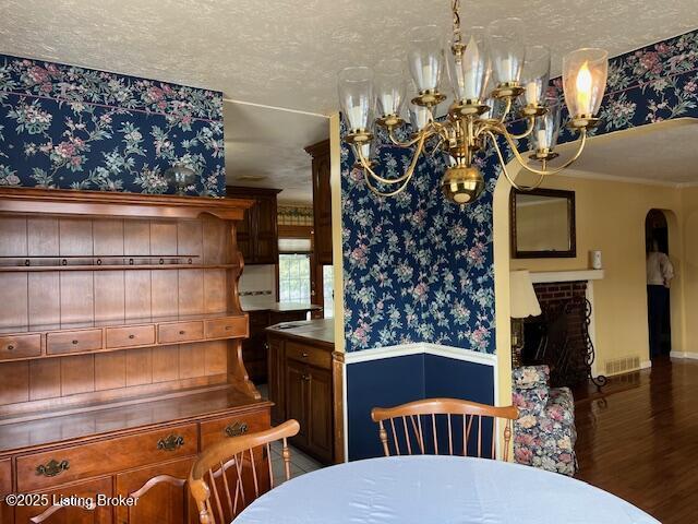 dining space with wood finished floors, baseboards, wallpapered walls, a chandelier, and arched walkways
