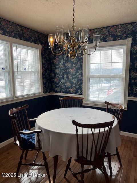 dining space featuring a textured ceiling, a chandelier, hardwood / wood-style floors, wallpapered walls, and baseboards
