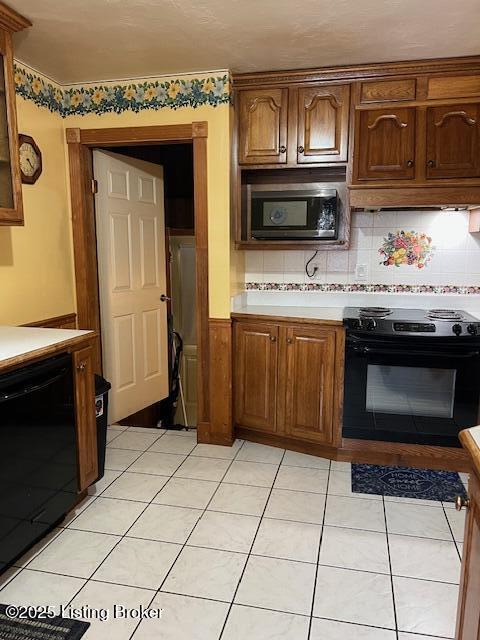 kitchen with light countertops, under cabinet range hood, black appliances, and tasteful backsplash
