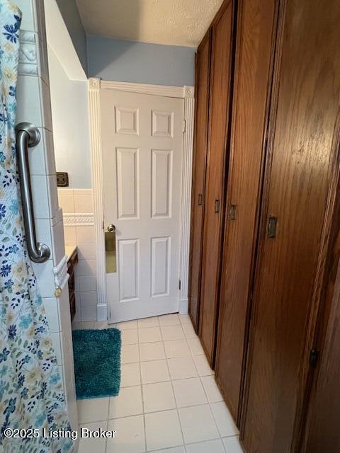 hallway with light tile patterned floors, tile walls, wainscoting, and a textured ceiling