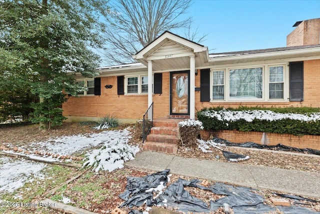 view of front of house featuring entry steps, a chimney, and brick siding